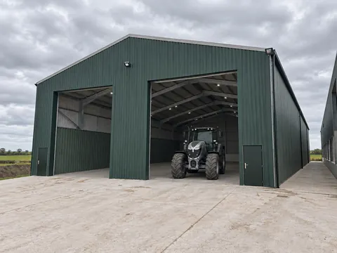 A green clad agricultural building with a tractor in the doorway