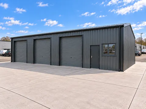 A dark clad steel framed building with three roller shutter doors and a window
