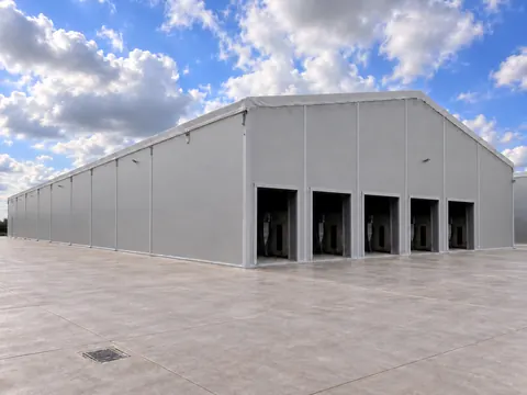 A temporary building seen across a concrete yard, roller doors open